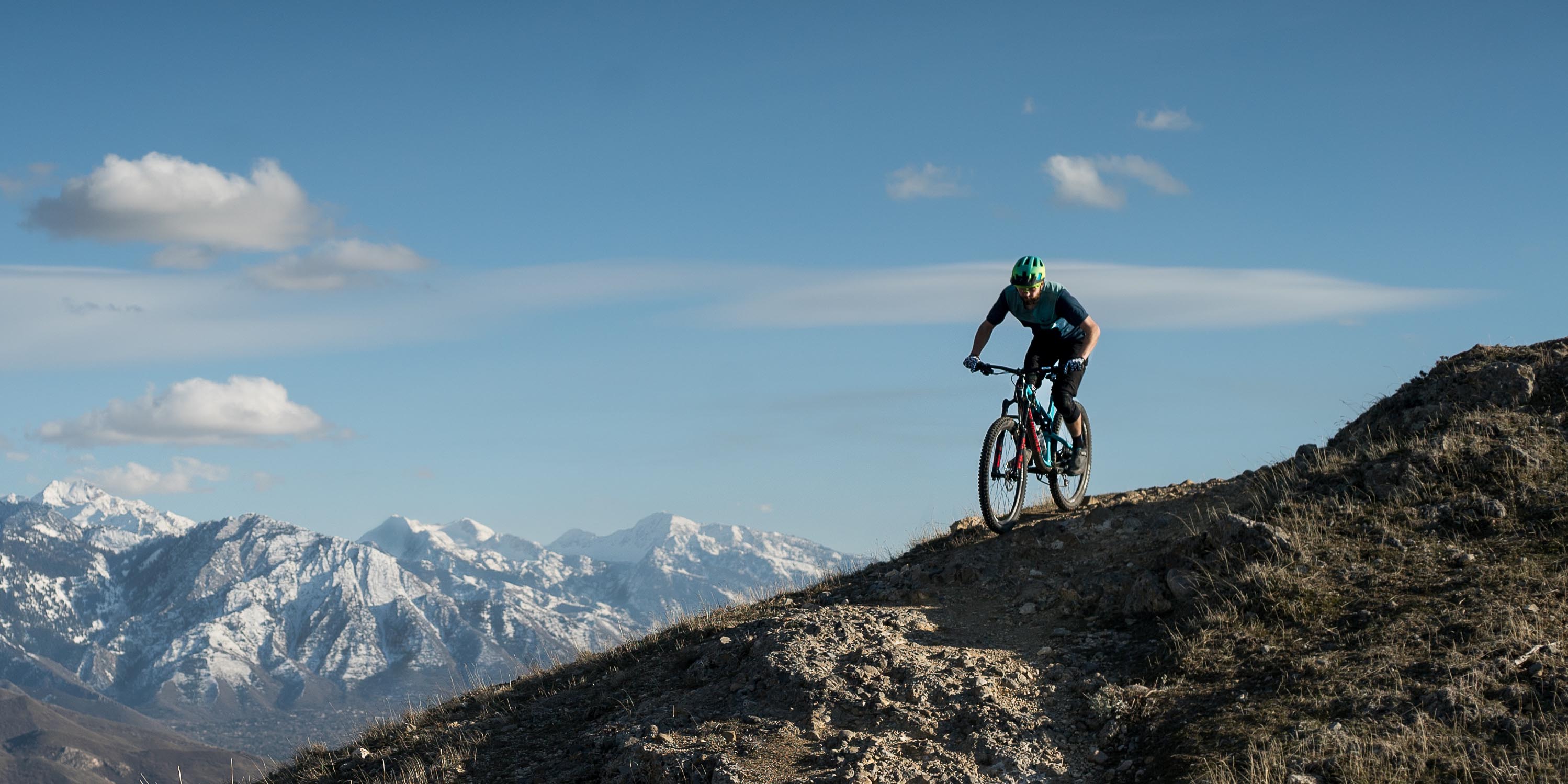 Mountain bike rider descending a ridgeline with snow-capped peaks in the background
